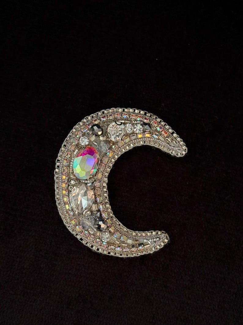 May include: A silver crescent moon brooch with iridescent and clear rhinestones.