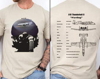 May include: A beige t-shirt with a black and white illustration of a pilot in a cockpit with an A-10 Thunderbolt II "Warthog" aircraft. The back of the shirt has a diagram of the aircraft with specifications.
