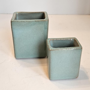 May include: A white ceramic mug with a black handle and the text "But First, Coffee" in a bold, black font. The mug is set against a blurred background, suggesting a cozy setting.