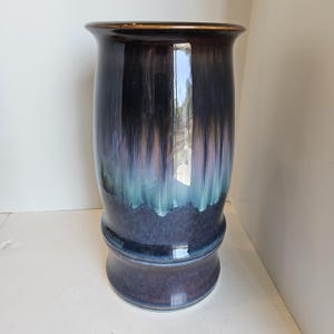 May include: A tall, glazed ceramic vase with a dark, iridescent finish. The vase features a flared rim and a bulbous base. The colors transition from dark blue to teal and brown, with a glossy sheen. The vase is approximately 12 inches tall.