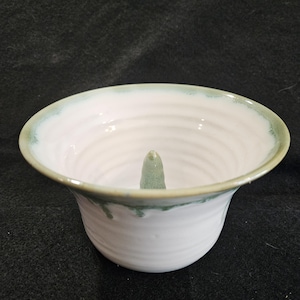 May include: A white ceramic apple corer with a green glaze. The corer has a central spire and a wide, shallow bowl.