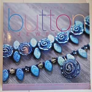 May include: A book cover titled "Button Jewelry" by Sara Withers. The cover features a collection of blue jewelry designs, including necklaces and earrings. The text "OVER 25 ORIGINAL DESIGNS FOR NECKLACES, EARRINGS, BRACELETS AND MORE" is at the bottom.