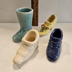 May include: Four ceramic shoe-shaped planters in different colors: blue, white, yellow, and dark blue. The planters are all small and have a simple design.