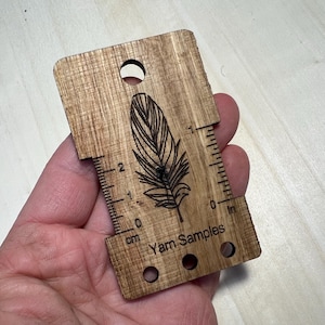 Könnte beinhalten: Holz-Garnmesser mit Federdesign, einem Lineal in Zoll und Zentimetern und dem Text "Yarn Samples".