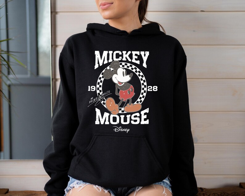 Op de afbeelding: Zwart hoodie met een vintage Mickey Mouse-print. De print toont Mickey Mouse in een rood-witte outfit, staand in een cirkel met de tekst "Mickey Mouse" en "1928" eromheen geschreven. De tekst "Disney" staat onder de cirkel.