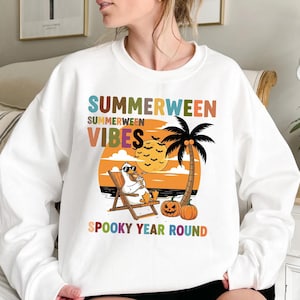 May include: White sweatshirt with the words "SUMMERWEEN VIBES" in colorful letters. The graphic features a duck in sunglasses relaxing on a beach chair, with a palm tree, pumpkins, and a full moon.