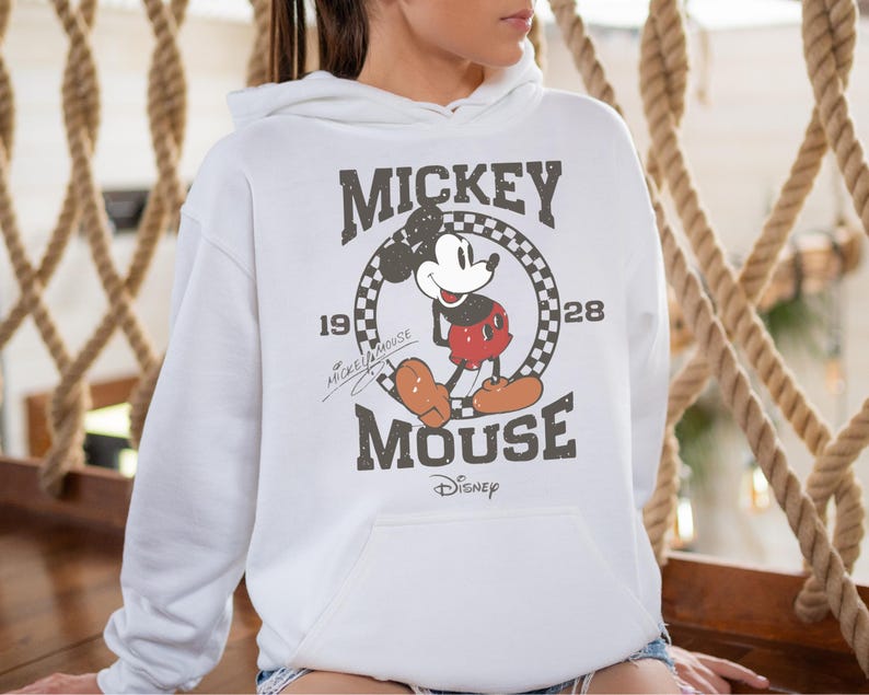 Op de afbeelding: Witte hoodie met een vintage Mickey Mouse-afbeelding. De afbeelding toont Mickey Mouse in een rood-witte outfit met de tekst "Mickey Mouse" en "1928" in een zwart-wit geblokte cirkel.