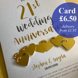 May include: A white 21st wedding anniversary card with gold lettering and six gold heart embellishments. The card includes the names "Stephen & Angela" and the date "28/09/2000".