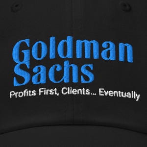 May include: Black baseball cap with the embroidered text "Goldman Sachs" in blue, with the tagline "Profits First, Clients... Eventually" in white. The cap has a curved brim and a button on top.