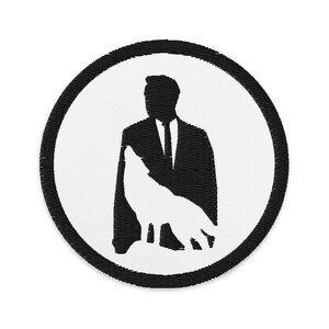 May include: Black and white embroidered patch of a man in a suit with a wolf silhouette behind him. The patch is circular with a black border.