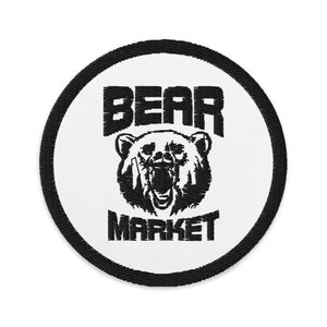 May include: A circular embroidered patch with a white background and a thick black border. The design features a black graphic of a roaring bear head centered between the words BEAR at the top and MARKET at the bottom in black text.