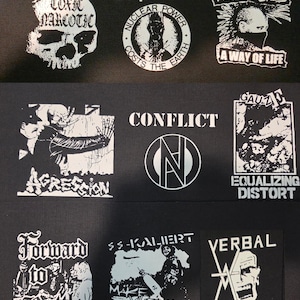May include: A collection of nine black fabric patches featuring white screen-printed graphics and text. The designs include band names and logos such as Toxic Narcotic, Oi Polloi, Funeral Dress, Agression, Conflict, Gauze, Forward to Battle, SS-Kaliert, and Verbal Abuse.