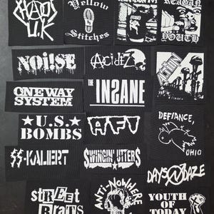 May include: A collection of black and white patches featuring band names and punk rock imagery. The patches display text like "Chaos U.K.", "Acidiz", "U.S. Bombs", and "Swingin' Utters", along with various graphics.
