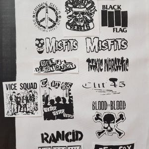May include: A collection of black and white punk rock band patches, including "Misfits," "Black Flag," and "Whiskey Rebels." The patches feature various graphics such as skulls, peace signs, and band names, all printed on a white fabric background.