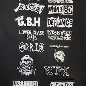 May include: A black background displays multiple white patches with band logos and names. Logos include "TOTAL CHAOS", "NOFX", "G.B.H", "MONSTER SQUAD", "GORILLA BISCUITS", and "CHEAP SEX". The patches vary in size and shape.