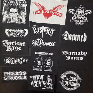 May include: A collection of black and white punk rock patches featuring band logos and graphics. Patches include "Cock Sparrer" with a red wing design, "The Damned", "The Varukers", and "Broken Cuffs".