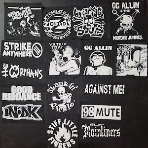 May include: A collection of black and white patches featuring band logos and graphics. The patches include text such as "HAVOC", "STRIKE ANYWHERE", "GG ALLIN", and "AGAINST ME!". The patches are square or rectangular.