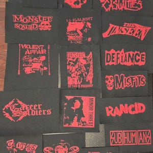 May include: A collection of rectangular black fabric patches featuring red screen-printed graphics and band logos including A Global Threat, Toxic Narcotic, Charged G.B.H, The Casualties, Monster Squad, SS-Kaliert, The Unseen, Violent Affair, Defiance, Misfits, Career Soldiers, Minor Threat, Rancid, Subhumans, Clit 45, Lower Class Brats, and Agression.