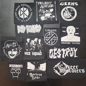 May include: A collection of black and white punk rock patches featuring band names and graphics. Patches include "Dead Kennedys," "Bad Brains," "Germs," "Crass," "Descendents," and "Career Soldiers."