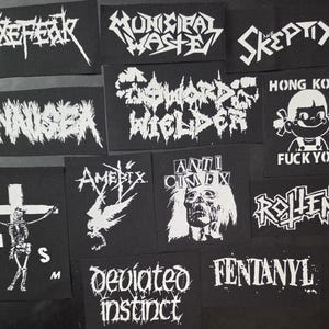 May include: A collection of black patches with white text and graphics. The patches feature band names like "Axefear", "Municipal Waste", and "Skeptix", along with other designs and phrases. The patches are rectangular and vary in size.
