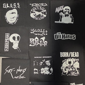 May include: A collection of black fabric patches featuring white screen-printed graphics and text, including band names like X-Ray Spex, G.L.O.S.S., The Ejected, Ajax, Subhumans, The Die Hards, Born/Dead, Surf-Nazis Must Die, and The Queers.