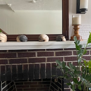 May include: A brick fireplace with a white mantel and a plant in a white pot. There are four small ceramic objects on the mantel, two are black and white and two are beige.