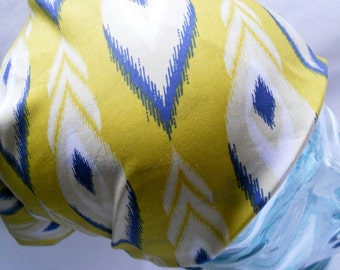 May include: A yellow fabric with a white and blue feather-like pattern is draped over a clear, light blue glass object. The fabric's design features repeating shapes in yellow, white, and blue. The glass object has a curved shape.
