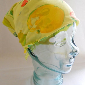 Puede incluir: Un pañuelo amarillo con estampado floral de limones y fresas. El pañuelo está atado en una cabeza de maniquí.