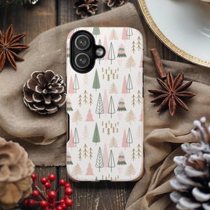 May include: A white phone case with a repeating pattern of stylized pink, green, and gold trees. The case has a gold-colored border and a black camera module. The case is surrounded by seasonal decorations.