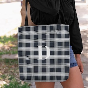 Puede incluir: Un bolso tote a cuadros azul marino y blanco con una gran letra "D" blanca en el centro. El bolso tiene una correa para el hombro. La persona que lleva el bolso lleva una camiseta negra y pantalones cortos vaqueros.