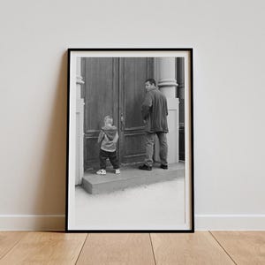 Pode incluir: Uma fotografia a preto e branco de um homem e um menino pequeno em pé em frente a uma porta. O homem está a usar uma jaqueta e calças, e o menino está a usar uma jaqueta e calças. O homem está a olhar para o menino, e o menino está a olhar para a porta.