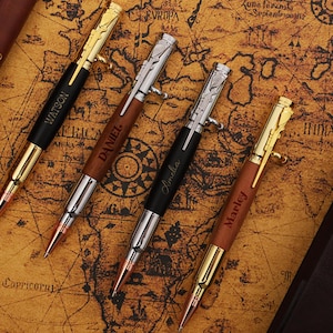 May include: Four personalised pens with a bullet design, featuring gold, silver, and black accents. Each pen is engraved with a name: Watson, Daniel, Amelia, and Marley. The pens rest on a vintage map.