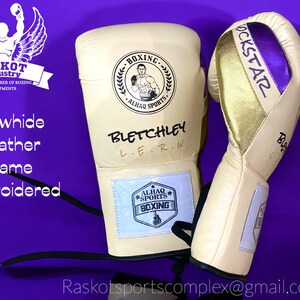 May include: A pair of beige boxing gloves with black and gold accents. The left glove has the text "BLETCHLEY L.E.R.W." and a logo with the text "ALHAQ SPORTS BOXING". The right glove has the text "ROCKSTAR" in gold and purple lettering. The gloves are on a purple background.