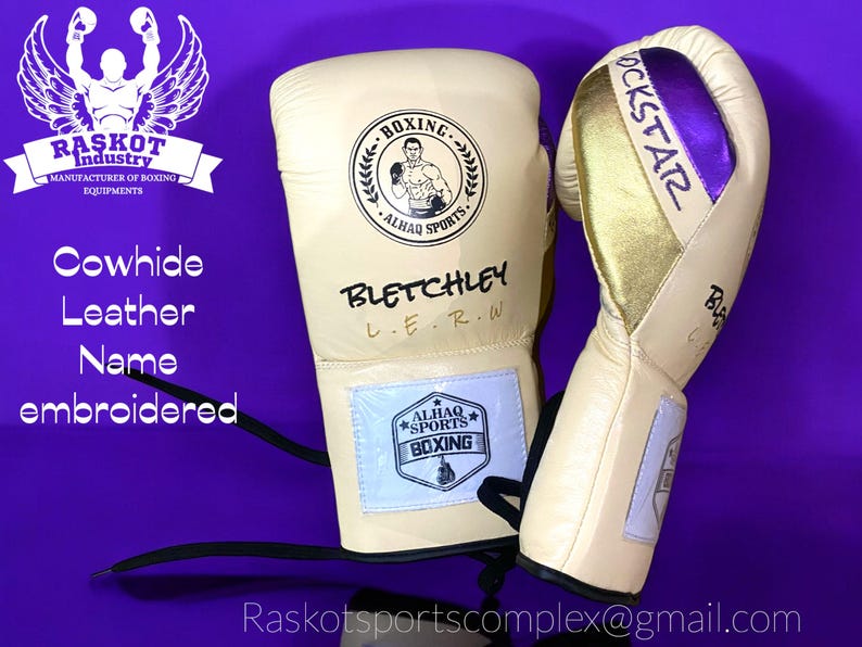 May include: A pair of beige boxing gloves with black and gold accents. The left glove has the text "BLETCHLEY L.E.R.W." and a logo with the text "ALHAQ SPORTS BOXING". The right glove has the text "ROCKSTAR" in gold and purple lettering. The gloves are on a purple background.