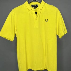 May include: A bright yellow polo shirt with a small black embroidered laurel wreath logo on the chest.
