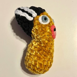 May include: A handmade, plush sculpture in the shape of a stylized face. The sculpture features a black and white striped hair, a yellow body, a blue eye, and a pink mouth. The texture appears soft and fuzzy.