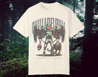 May include: White t-shirt with a green and black graphic of a football player holding two eagles and a panther. The text "PHILADELPHIA" is above the graphic and "PASSION. GRIT. FOOTBALL" is below.