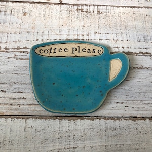 May include: A blue ceramic coffee cup dish with a white rim and handle. The dish has a speckled glaze and says "coffee please" in black lettering.