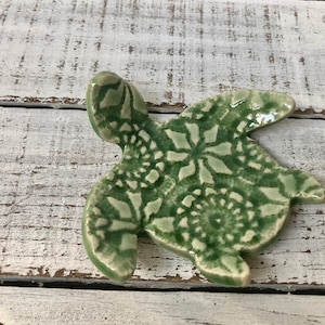 May include: A green ceramic turtle dish with a white floral design. The dish is perfect for holding small items like jewelry or keys.