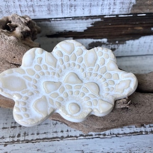 May include: A white ceramic dish with a lacy design. The dish is shaped like a cloud and has a raised edge.