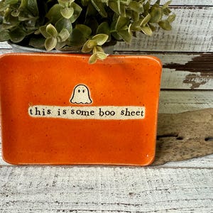 Peut inclure: Plat rectangulaire en céramique orange avec une illustration de fantôme et l'expression "this is some boo sheet". Le plat est décoré d'un fantôme blanc et de texte sur fond blanc.