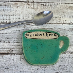 May include: A green ceramic spoon rest shaped like a coffee cup with the text "witches brew" on the side.