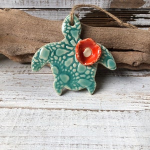 May include: A teal green ceramic turtle ornament with a textured shell and a red flower on its back.