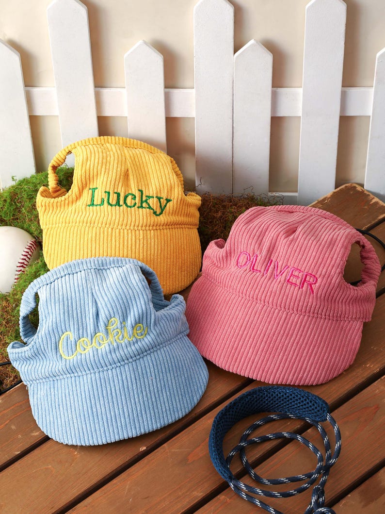 May include: Three corduroy pet hats in yellow, light blue, and pink. The yellow hat features the green embroidered text Lucky, the light blue hat has yellow embroidered text Cookie, and the pink hat has red embroidered text OLIVER.