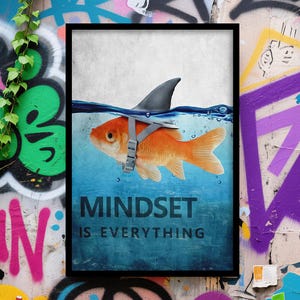 Può includere: Un poster incorniciato con un pesce rosso con pinna di squalo e imbracatura in acqua blu. Il testo bianco recita "MINDSET IS EVERYTHING". Lo sfondo è un muro coperto di graffiti.
