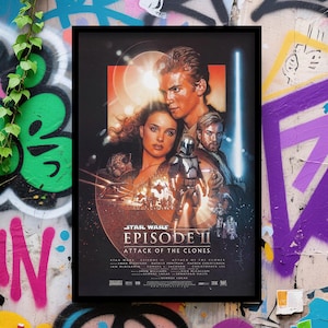 May include: A framed movie poster for Star Wars: Episode II - Attack of the Clones. The poster features Anakin Skywalker, Padmé Amidala, Obi-Wan Kenobi, and a Mandalorian. The title is prominently displayed with the film's title and credits at the bottom.