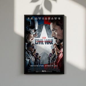 K&ouml;nnte beinhalten: Ein gerahmtes Filmplakat f&uuml;r Marvel's Captain America: Civil War. Das Poster zeigt Captain America und Iron Man einander gegen&uuml;ber. Der Titel "CIVIL WAR" ist deutlich zu sehen. Der Slogan "UNITED WE STAND. DIVIDED WE FALL." ist ebenfalls sichtbar.