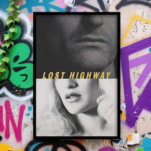 May include: Black framed poster with a black and white image of a man and woman's faces. The text "LOST HIGHWAY" is in gold lettering. The poster is displayed against a graffiti wall.