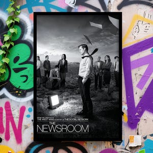 Op de afbeelding: Zwart-wit poster voor "The Newsroom" in een zwarte lijst. De poster toont een groep mensen die in een veld staan, met een man op de voorgrond. De tekst op de poster luidt "From the creator of The West Wing & writer of The Social Network".