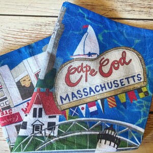 May include: A blue and white beach towel with a red and white "Cape Cod, Massachusetts" sign, a lighthouse, a sailboat, and a red and white house.